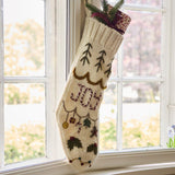 Christmas stocking with 'Joy' embroidery hanging on a window, filled with gifts, adding a festive and cheerful touch to holiday decor.