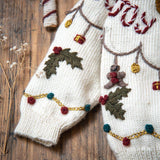 Detail view of the cream white sweater's knitted fabric, illustrating the softness and high-quality craftsmanship of the hand-embroidered holiday designs.