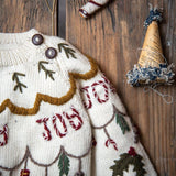 Close-up of the cream white Joy Sweater, highlighting the intricate hand-embroidered holiday motifs including candy canes and gifts.