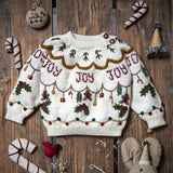 Christmas Joy Sweater in cream white displayed on a wooden surface, set in a festive Christmas environment, showcasing the luxurious hand-embroidered holiday motifs amidst seasonal decorations.