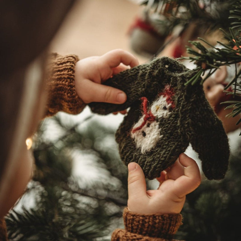 child holding a knitted green sweater ornament with hand embroidered snowman on it