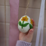 Hand holding a felted ornament with a flower design against a neutral background