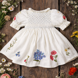White dress with floral embroidery on a wooden surface surrounded by flowers