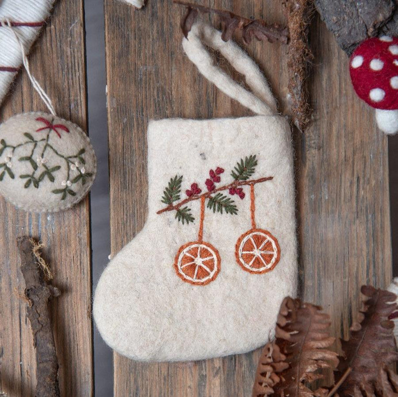 Mini Stocking with hand-embroidered orange motif, displayed in a festive Christmas setting. Surrounded by holiday decorations, the stocking's detailed embroidery and seasonal charm are highlighted.