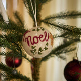 Bauble Noel Ornament adorned with holiday motifs, hanging from a Christmas tree, adding a touch of handcrafted elegance and festive spirit to the tree.