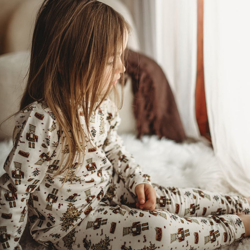 Child wearing a patterned pajama set sitting on a bed.