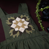 close up of green patchwork romper for kids on grape background surrounded with fruit and plants