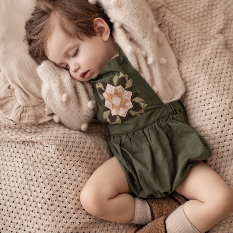 sleeping child in a patchwork green romper and knitted popcorn sweater