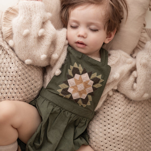sleeping child in a patchwork green romper and knitted popcorn sweater