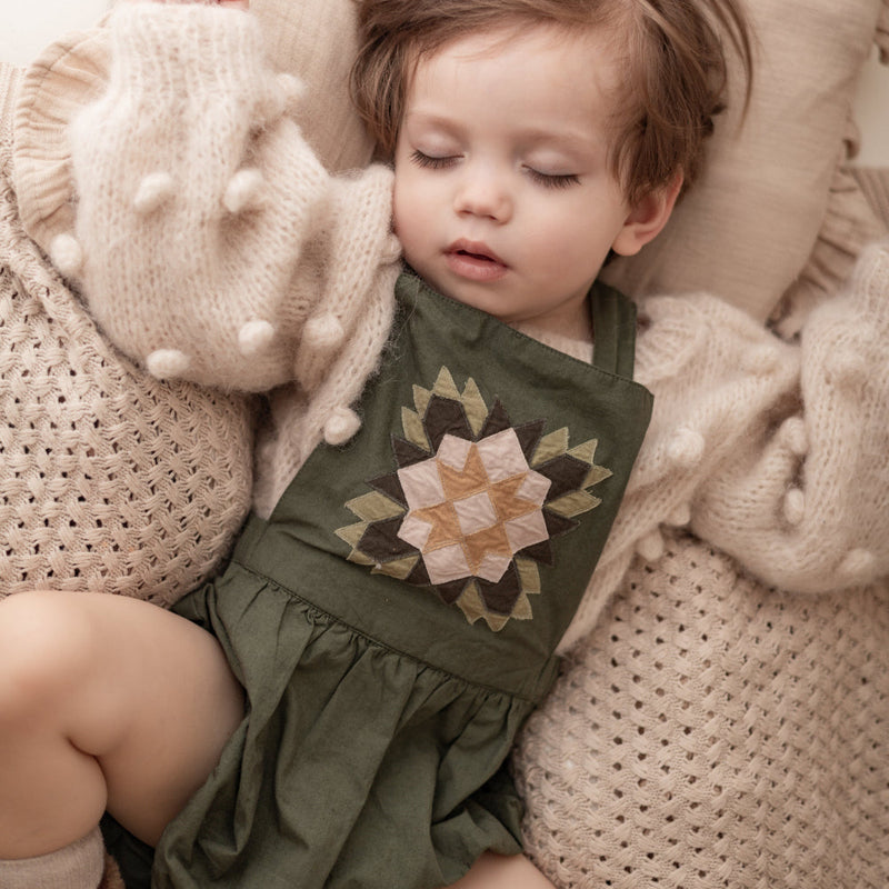 sleeping child in a patchwork green romper and knitted popcorn sweater
