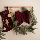Decorative Christmas stockings and wreath hanging on a wall with a framed picture above.