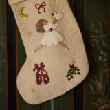 Handcrafted cream white stocking featuring embroidered Odette, resting on a wooden surface, showcasing its intricate design and 100% wool material.