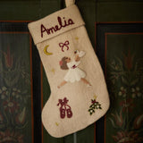 Handcrafted cream white stocking featuring personalized embroidered Odette, resting on a wooden surface, highlighting its detailed design and 100% wool material.