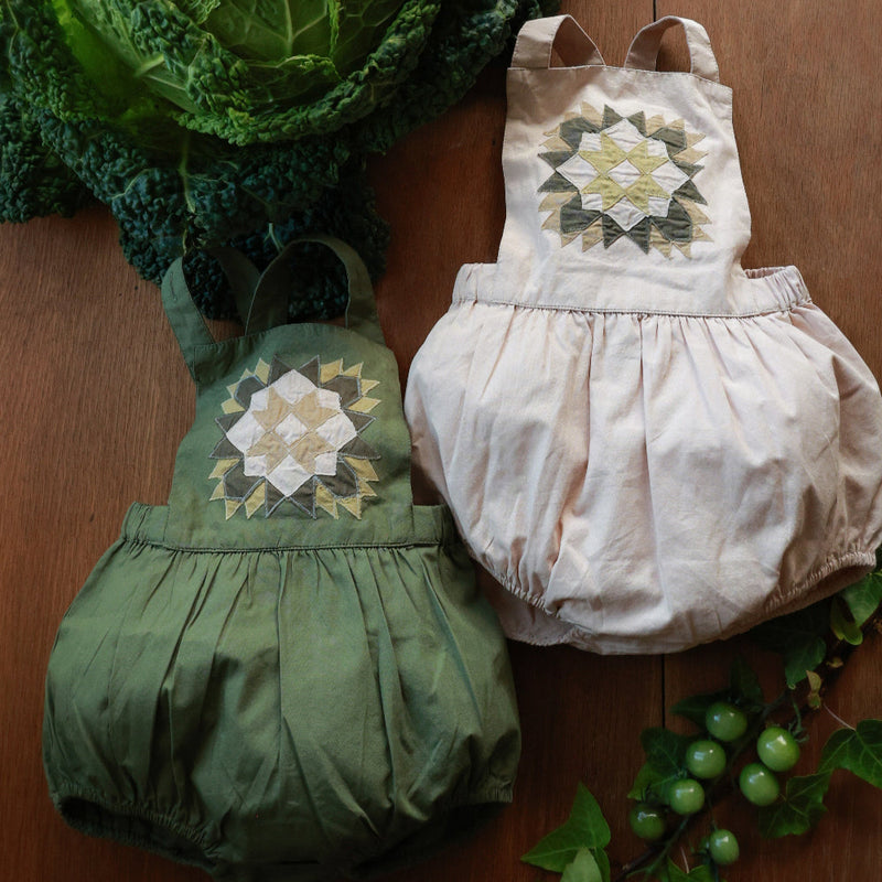 Green and beige baby romper with patchwork patterns on a wooden surface