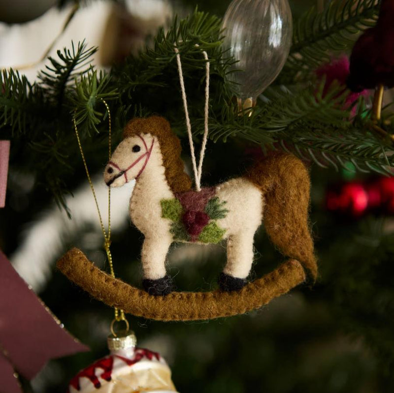 Hand-felted rocking horse ornament on a Christmas tree, surrounded by other holiday decorations. The ornament adds nostalgic charm and whimsy to the festive setting.