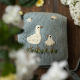 Knitted pouch with embroidered birds surrounded by flowers on a wooden surface