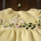 Yellow fabric with embroidered birds and flowers on a wooden surface.