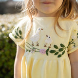 Child wearing a yellow embroidered dress with birds and flowers outdoors