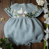 Light blue knitted baby romper with duck and floral embroidery on a wooden surface with flowers.