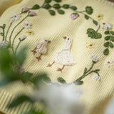 Embroidered fabric with ducks and floral patterns on a yellow background