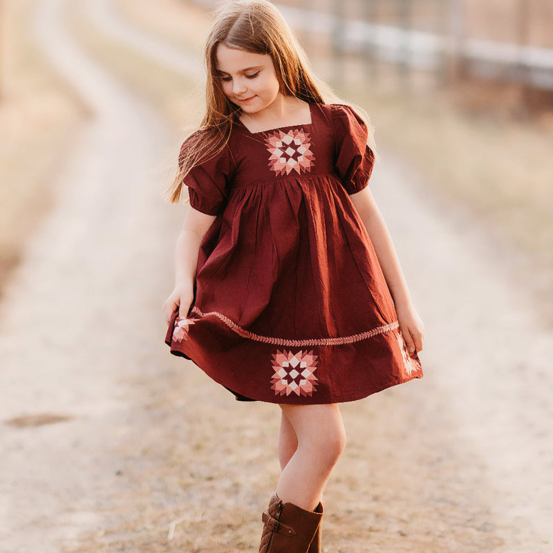 Young girl in a red dress with floral patterns standing on a road.