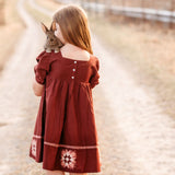 Girl in a red dress holding a rabbit on a dirt road