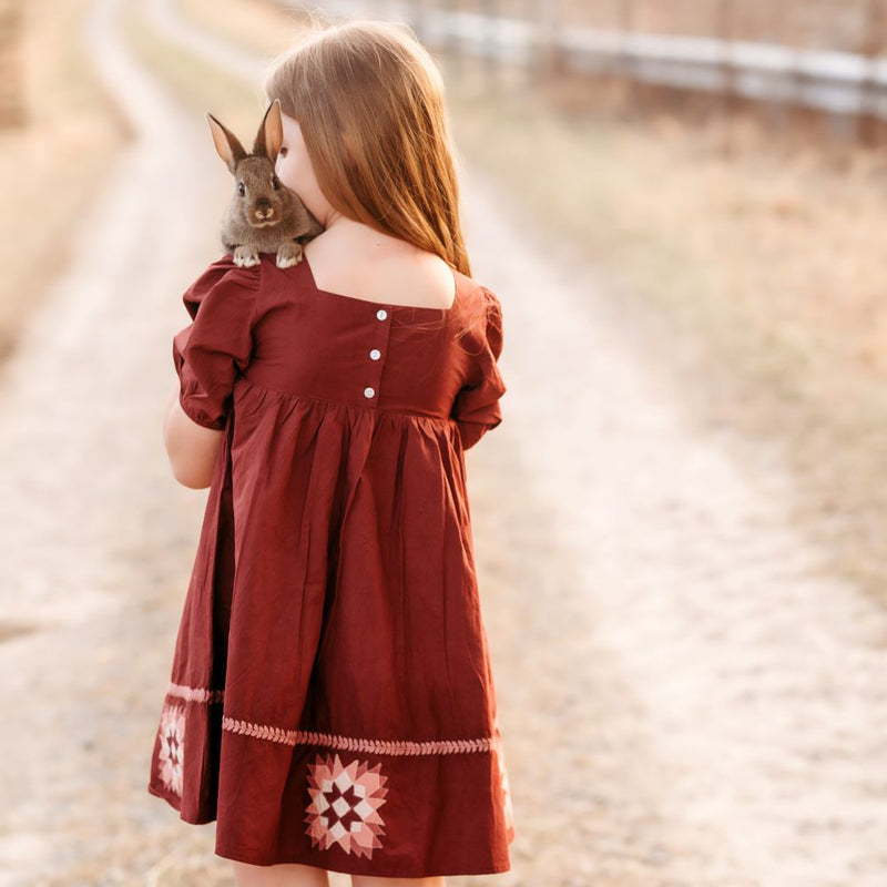 Girl in a red dress holding a rabbit on a dirt road