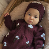 baby in knitted and embroidered hellebores romper and bonnet