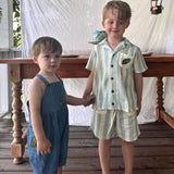 Two children on the picture, with a wooden table in the background, one child wearing the Ladybird dungaree.







