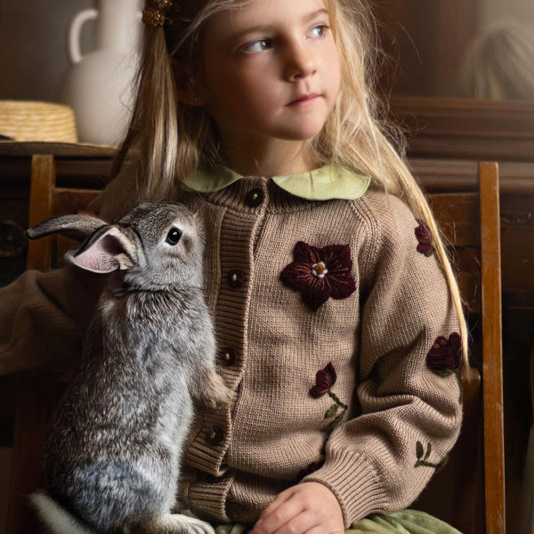 a girl wearing knitted and embroidered hellebores cardigan and holding a rabbit