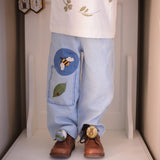 a boy wearing blue pants with embroidered bee and a leaf