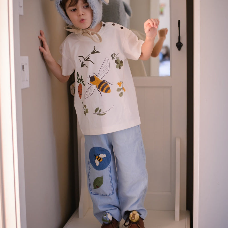 a boy wearing blue pants with embroidered bee and a leaf and also a bee shirt