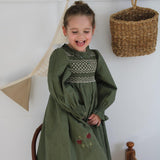 girl in green sewn dress with smock and flower embroidery standing on a chair