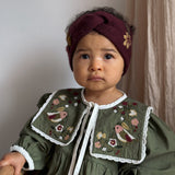 child in a green romper with embroidered collar and grape knitted hairband