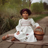 girl in white dress with flower embroidery sitting on a blanket