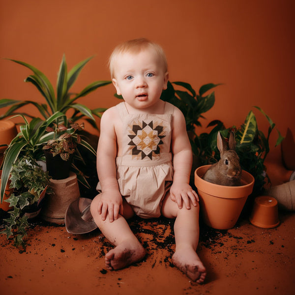 baby posing between plants in a patchwork romper