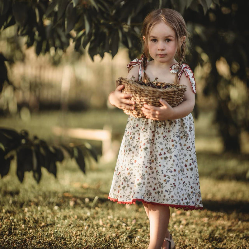 Young girl in a floral dress holding a basket of leaves in a natural setting