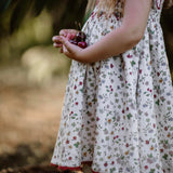 Child in a floral dress holding cherries in a natural setting