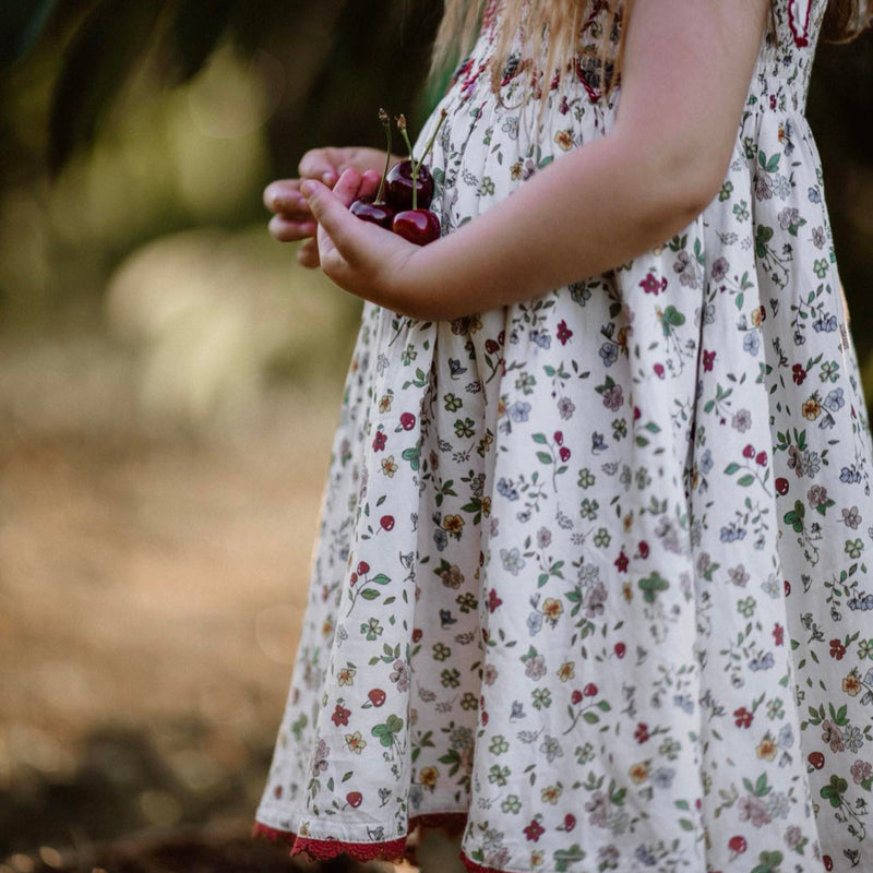 Child in a floral dress holding cherries in a natural setting