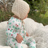 Baby in a clover outfit and knitted hat sitting on a blanket outdoors.