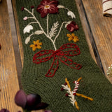 Green knitted stocking with floral embroidery on a wooden surface