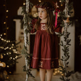 Young girl in a red dress standing on a fluffy rug with Christmas decorations in the background.