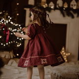 Young girl in a red dress standing in a festive room with Christmas decorations.