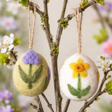 Decorative Easter eggs with floral designs hanging on a branch with flowers in the background