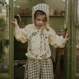 Child in a green and white checkered outfit standing inside a greenhouse.