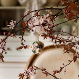 Decorative branches with pink flowers and a small ornament on a blurred background