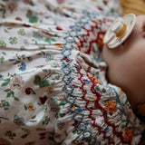 Close-up of a baby wearing a floral dress with a pacifier in mouth.