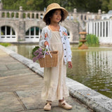 Child in a floral dress and hat standing by a pond with a stone bridge in the background