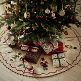 A decorated Christmas tree with red, gold, and white ornaments, wrapped in green and red ribbon presents underneath, and a round cream tree skirt with red trim on a light wood floor.