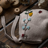 Knitted bonnet with floral patterns on a wooden surface with toys around